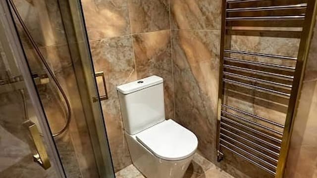 Bathroom completed by Kingdom Build with marble-effect tiling, brushed brass heated towel rail and a glass shower screen